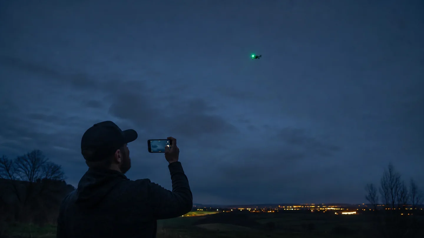 Observateur filmant un drone civil muni d'un feu vert à la tombée de la nuit, illustration éditoriale