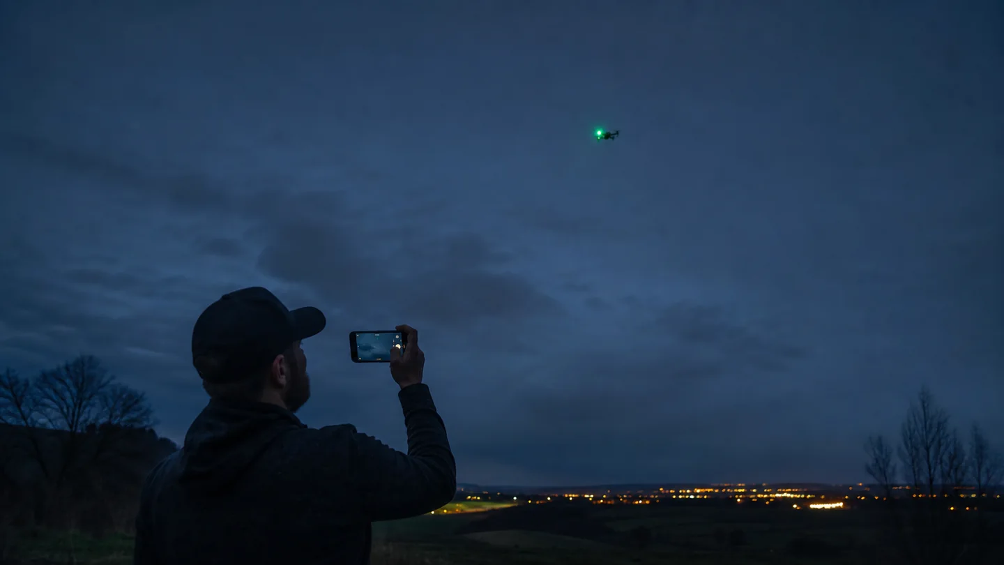 Observateur filmant un drone civil muni d'un feu vert à la tombée de la nuit, illustration éditoriale
